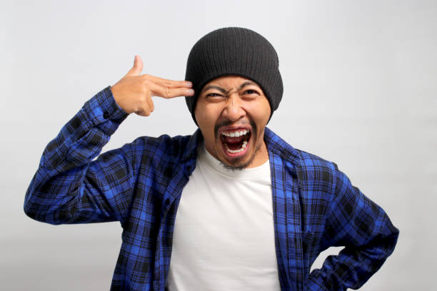istock Distressed young Asian man is showing finger pistol gestures above his head 1861299583