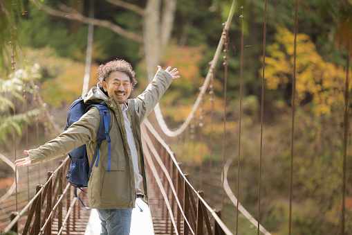 A happy man trekking and climbing a mountain, autumn scenery, looking at the camera. Fun-looking Asian man on an autumn excursion in Japan.