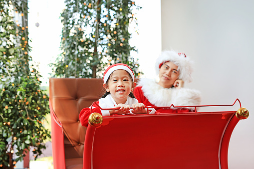 Happy little child girl and her mother in santa costume dress sitting on red sledge christmas background.  Merry Christmas and happy new year.