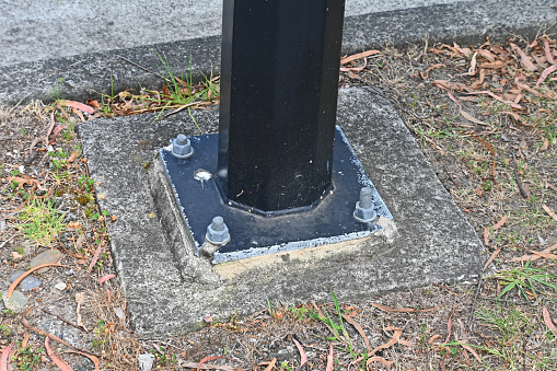 The base of a lamp  post that is bolted to the ground