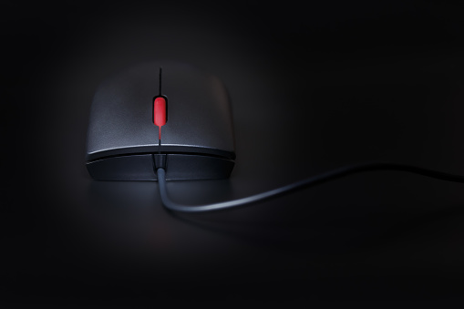 Black computer mouse with a red scroll wheel, close-up on a dark background with shallow depth of field