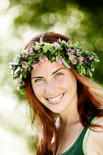 A young red headed woman wearing a flower crown looks at the camera and smiles