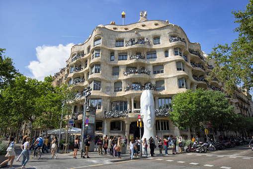 Street view of Casa Mila, Barcelona, Spain, Barcelona, Spain. Many people outside of the building around the intersection.