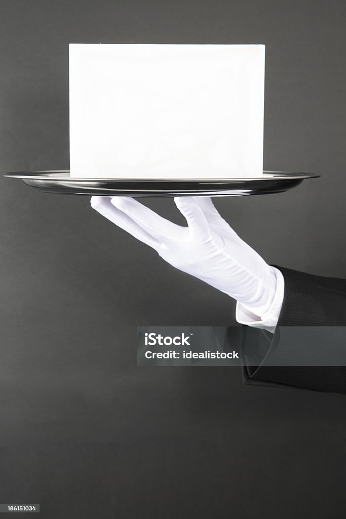 Announcement for You A butler or waiter holding a blank card on a silver platter in front of a dark wall. Luxury Stock Photo