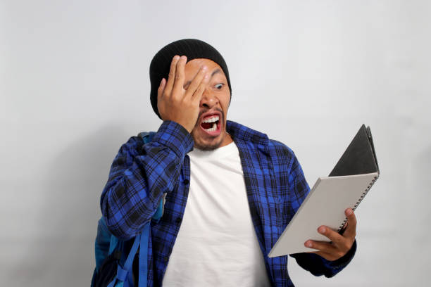 istock Asian student is peeking through his fingers shocked while reading his notebook 1861514502