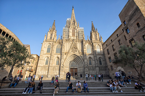 Exterior view of Cathedral of Barcelona in sunset light, Spain. Many people can be seen sitting on the stairs.