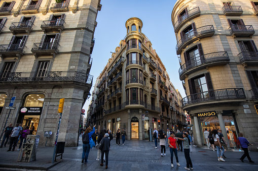View of crowded La Rambla street, Barcelona, Spain.  Tourists seen at an intersection in front of old style apartment buildings.