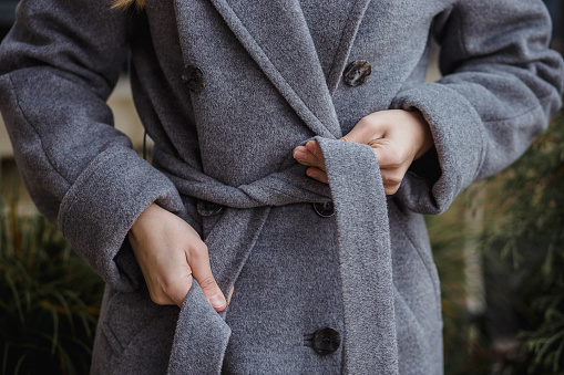 cropped shot of woman in wool coat tying belt.
