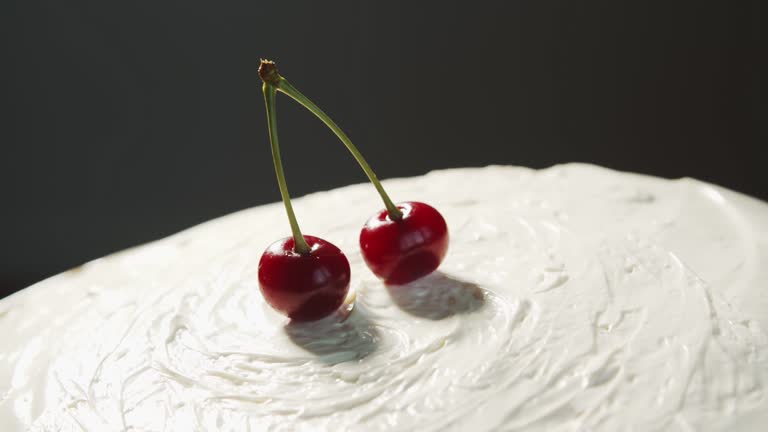 A hand puts two fused red cherries on a homemade white cake that rotates close-up