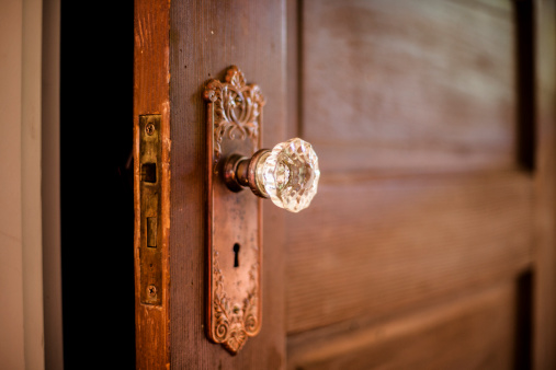 A weathered old wooden door with an ornate crystal door knob.