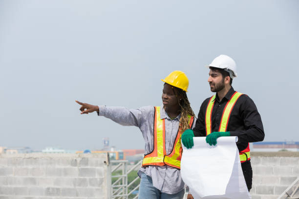 istock Foreman builder male and female at construction site. Group of foreman construction working at construction site, wearing safety uniform, helmet and holding blueprint structure 1861631674