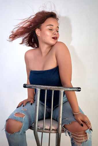 Girl sitting in a blue blouse and jeans with a white wall modeling