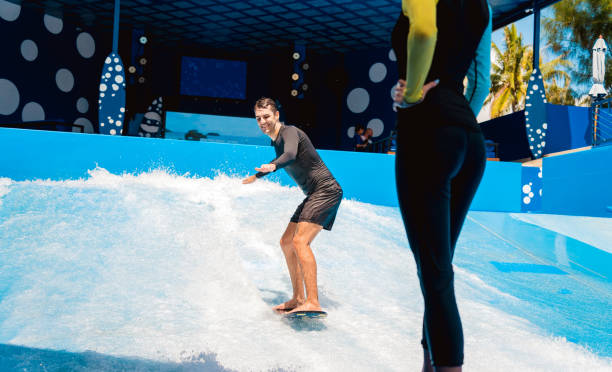 istock Young man surfing with trainer on a wave simulator at a water amusement park 1861640439