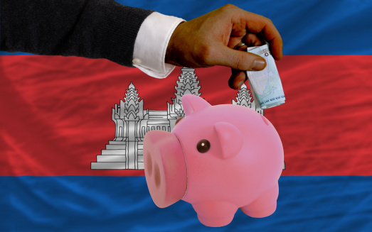 Man putting euro into piggy rich bank and national flag of cambodia in foreign currency because of insecurity and inflation