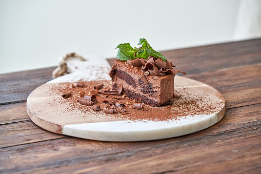 Delicious chocolate cake decorated with shavings and mint leaves placed on cutting board at wooden table
