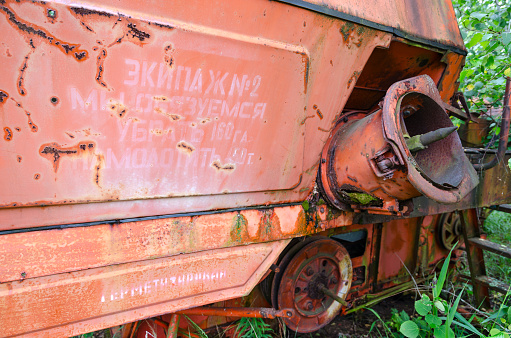 Inscription with socialist commitment on abandoned combine harvester at mechanical yard of state farm Victory of Socialism in resettled village of Pogonnoye in Chernobyl exclusion zone, Belarus. Inscription on harvester: Crew 2 We undertake to harvest 160 hectares and thresh 450 tons