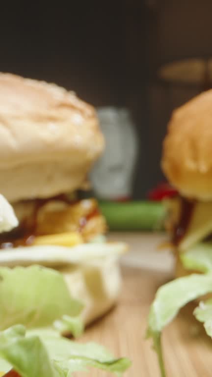 Vertical video. Vegetables and sauces for burgers behind on the table. The camera moves across the finished burgers. Not a healthy and fast food. Dolly slider extreme close-up.