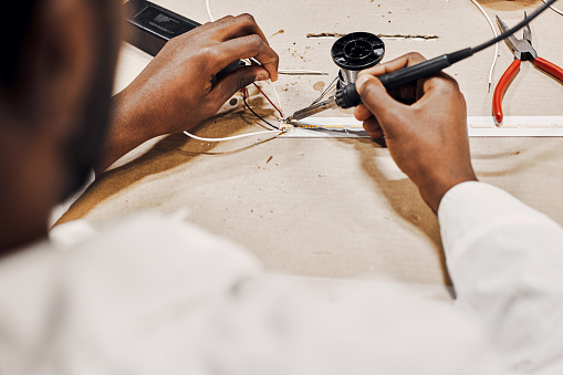 Close up of african man hands working with soldering iron, connecting LED lamps and wires. He is wearing white robe, workinf at the factory