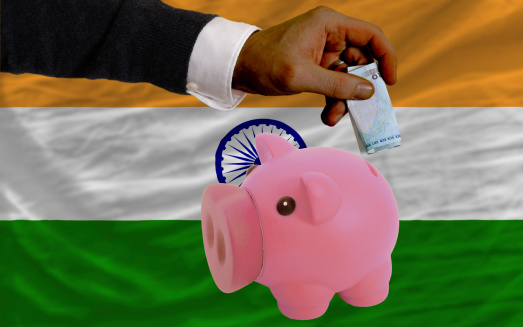 Man putting euro into piggy rich bank and national flag of  india in foreign currency because of insecurity and inflation