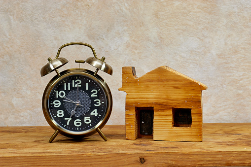 alarm clock and mini wooden house model on wooden table. time to Planning buy property. Choose what's the best concept