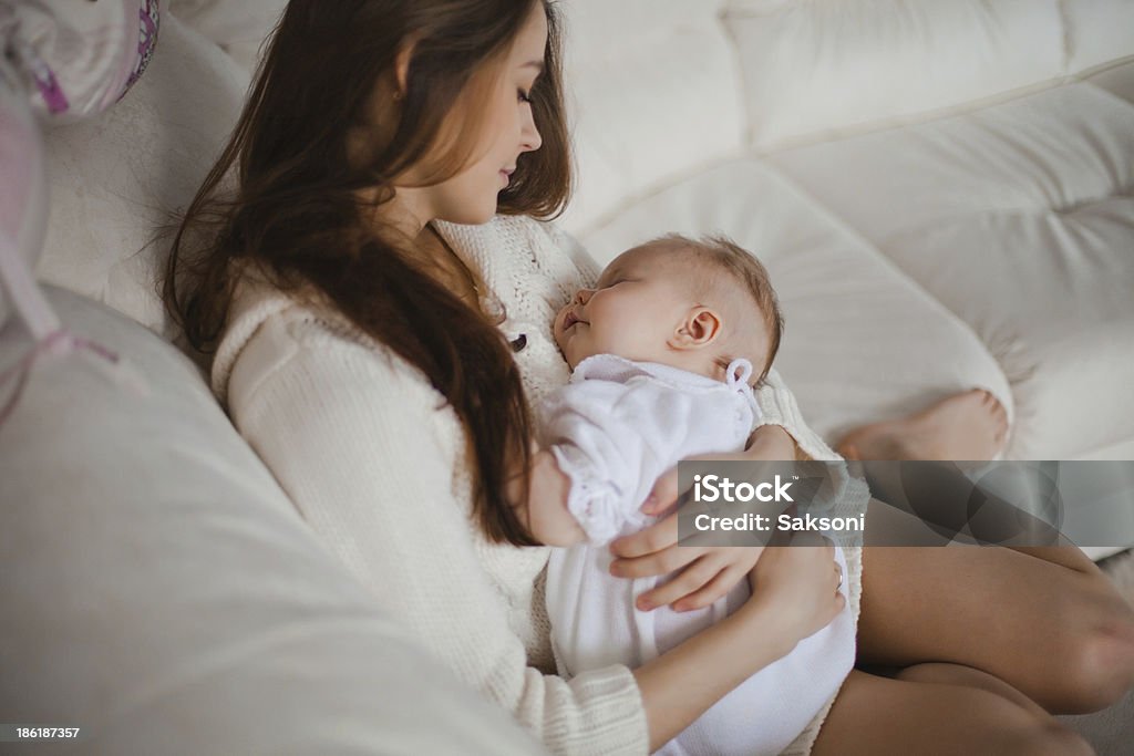 mother with baby Young caucasian mother taking care of her baby sitting on the sofa Adult Stock Photo