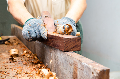 Carpenter's hands planing a plank of wood with a hand plane