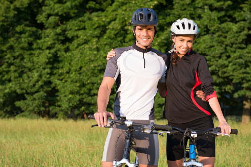 Portrait Of Young Sportive Couple With Bicycle In Meadow.