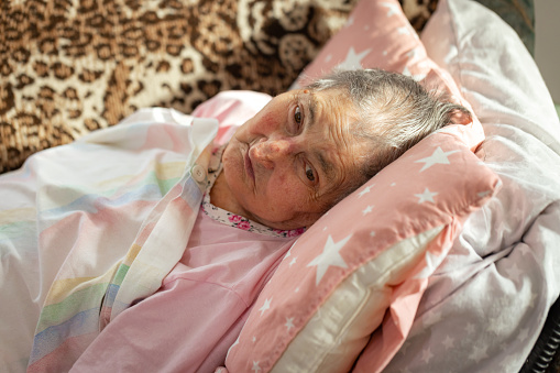 A tired elderly woman lays on a couch, tissues at hand, enduring illness in her living room.