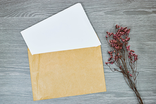 White envelope mock-up, blank template with yellow gypsophila flower on wooden gray table