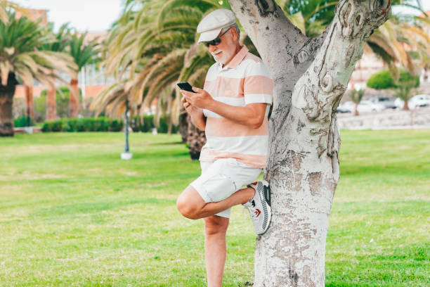 istock Smiling bearded senior man standing under a tree in public park using mobile phone. Relaxed elderly man holding telephone enjoying app and social media 1861946515