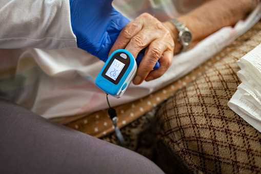 Nurse attentively measures oxygen levels in elderly patient's fingertip for vital health assessment.
