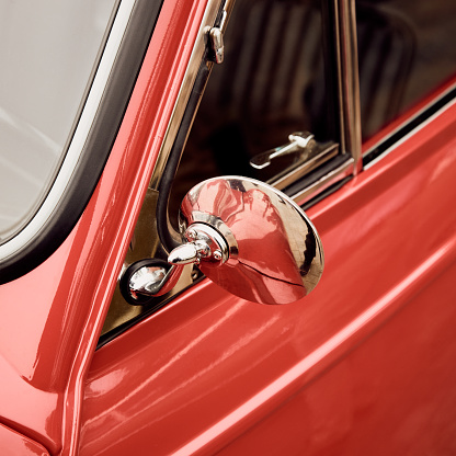 Close up of red classic car chrome rear view mirror.