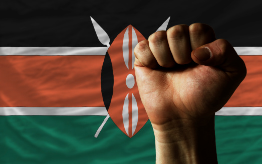 complete national flag of kenya covers whole frame, waved, crunched and very natural looking. In front plan is clenched fist symbolizing determination