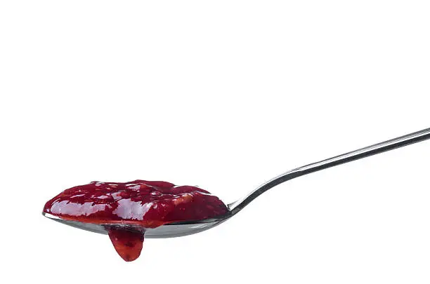 Raspberry jam dripping from a spoon isolated on white background