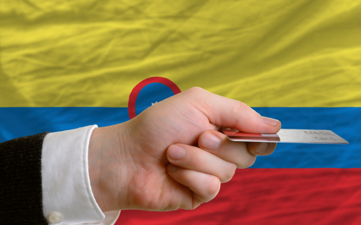 man stretching out credit card to buy goods in front of complete wavy national flag of colombia