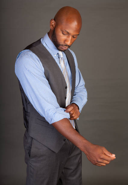 Young black business man on a grey background wearing a shirt tie and vest rolling his sleeves