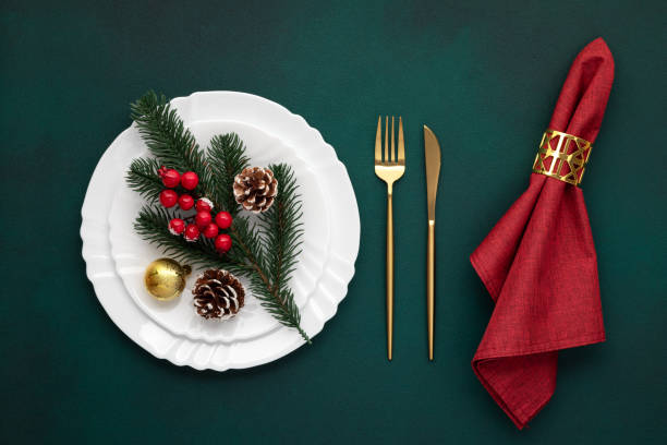 istock Christmas table setting. White plate, golden fork, knife. Pine tree branch and red napkin on green background. Invitation design. New Year's decorations. Top view. Luxury celebration dinner. 1861990892
