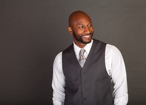 Young black business man on a grey background wearing a shirt tie and vest looking to his left or camera right