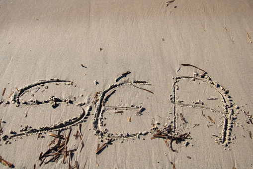 Word sea written in English on the sand on a beach bordering the waves