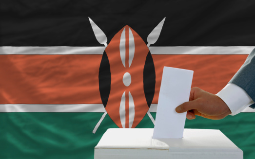 man putting ballot in a box during elections in kenya in fornt of flag