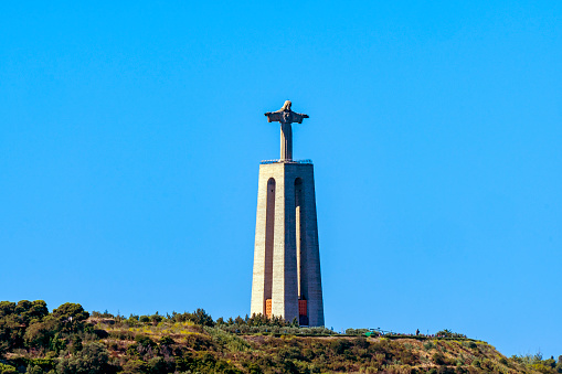 Panoramic view of the monumental stone Statue of Christ the King Almada of Lisbon (Christus Statue Lissabon), a sanctuary dedicated to the Sacred Heart of Jesus of Almada. Clear blue sky.