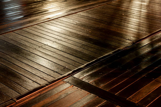 Abstract detail of a wooden boardwalk at night in the rain and illuminated by colorful, artificial lights.