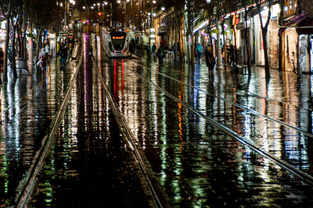 Abstract rendering of the slick pavement and tracks of the Jerusalem light rail illuminated by bright, colorful artificial light on a rainy winter night in Israel.