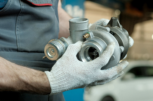 The new turbocharger is in the hands of an auto mechanic. View on the background of a repair shop in a car service station.