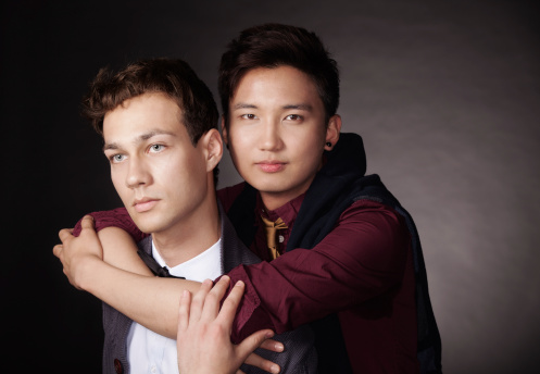 Two young fashion models embrace isolated on a black background.