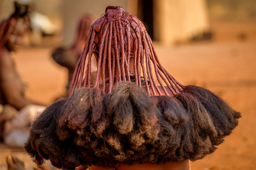 Namibia, Africa, September 22, 2017: A close up of a Himba Tribe woman's hairstyle seen in the arid landscape. The Himba are an indigenous Namibian nomadic tribe in northern Namibia. Women cover themselves and their hair with otjize paste, a mixture of butterfat and ochre pigment