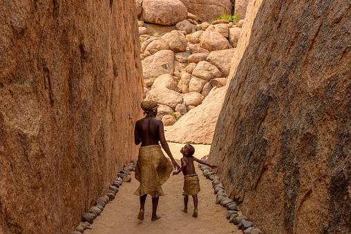 Damaraland, Twyfelfontein, Namibia, Africa, September 21, 2017: A Damara Tribe woman and a  child are seen walking away between two large rocks