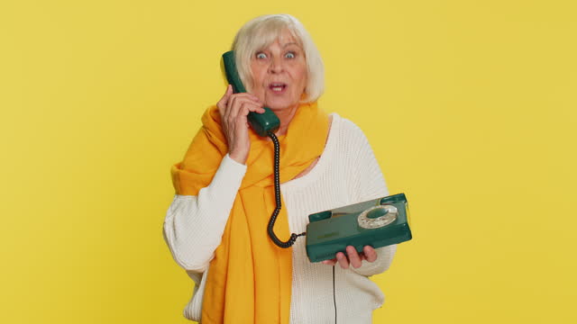 Senior woman talking on wired landline vintage telephone, advertising proposition of conversation
