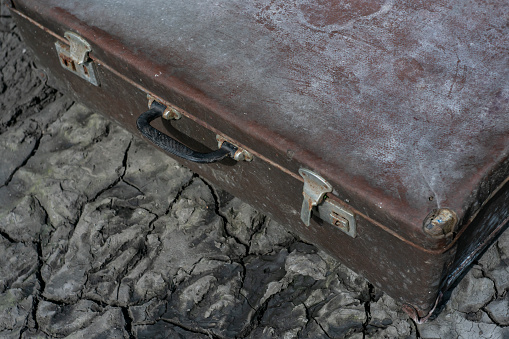 Old suitcase thrown out of the house on cracked gray soil