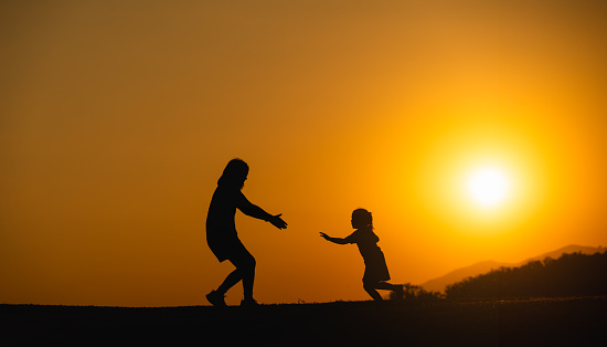 Silhouette, happy mother and daughter running to hug each other on the field lawn at sunset in the evening. Love family activity relax concept.